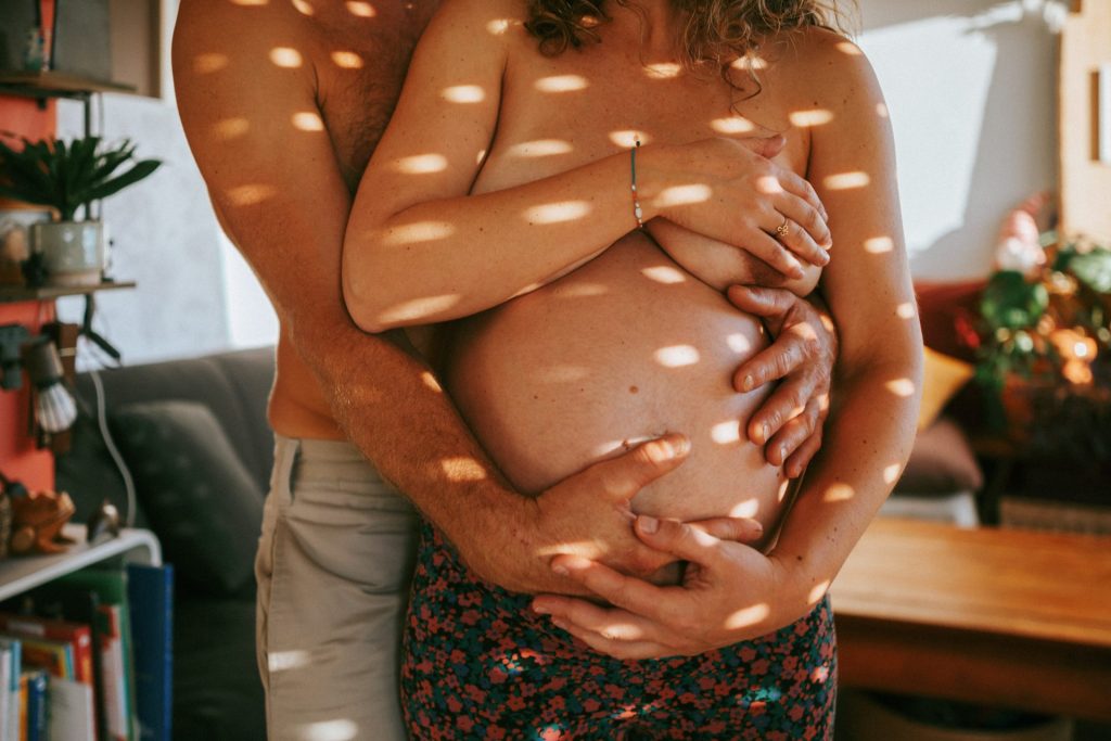 Couple enlacé dans une lumière naturelle, mettant en valeur un ventre de grossesse, capturé par une photographe dans les Landes et le Pays Basque.